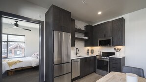 Una cocina compacta con refrigerador, estufa, microondas y gabinetes oscuros.