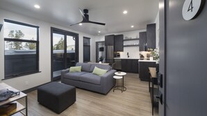 Una sala de estar moderna con un sofá gris, un pequeño otoman y un comedor con una mesa y sillas.