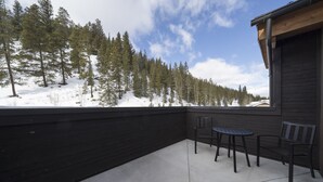 Un porche cubierto con una mesa y sillas, con vistas a un paisaje nevado con árboles.
