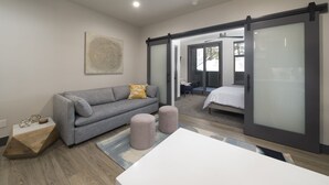 Un dormitorio moderno con un sofá gris, una cama blanca y un ventanal corredero que da a un balcón.