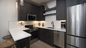 Una cocina moderna con armarios oscuros, electrodomésticos de acero inoxidable, una encimera blanca y un taburete de madera.