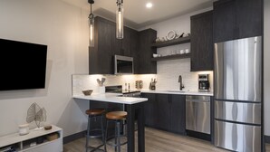Une cuisine moderne avec des meubles de couleur sombre, des appareils en acier inoxydable et un îlot central doté de tabourets.