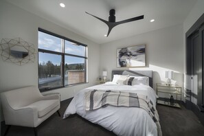 A modern bedroom with a large bed, a chair, a desk, and a view of a snowy landscape through a large window.