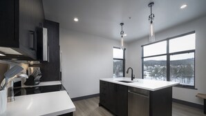 Una cocina moderna con armarios oscuros, encimera blanca, lavavajillas de acero inoxidable y un amplio ventanal con vistas a un paisaje nevado.