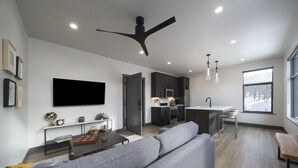 Una sala de estar moderna con un sofá gris, una mesa de centro y un televisor montado en la pared.