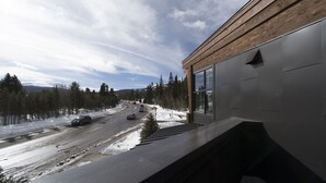 Un bâtiment moderne doté d’une façade en bois et de grandes fenêtres, qui offre une vue sur un paysage enneigé avec une route et des arbres.