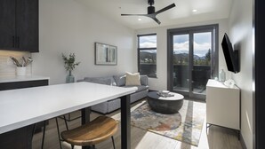 Une cuisine moderne avec un plan de travail blanc, des meubles de couleur sombre et un coin repas agrémenté d’une chaise en bois.