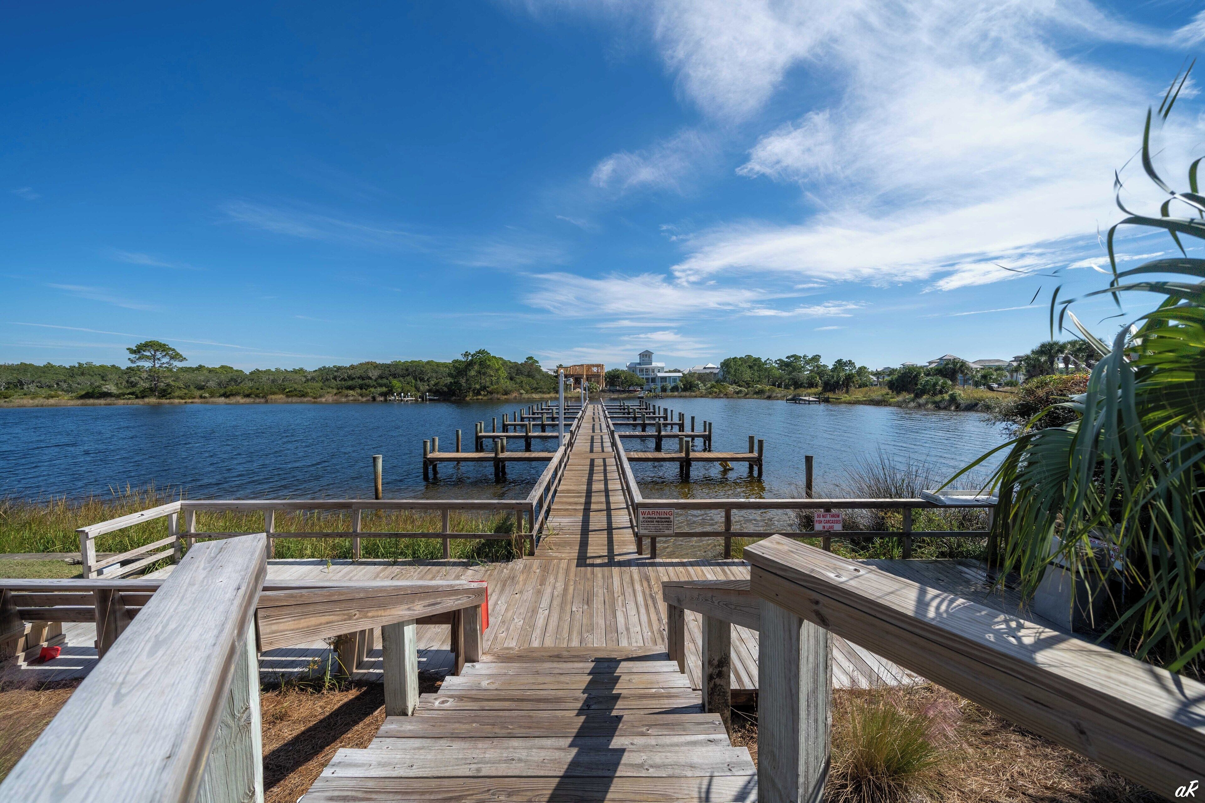 A wooden pier leading to a dock with a view of a lake and distant buildings.