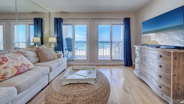 A living room with a sofa, a coffee table, a wooden dresser, and a large window with a view of the beach. - End of Summer Sunset Views PPC3-401 (Panama City Beach)