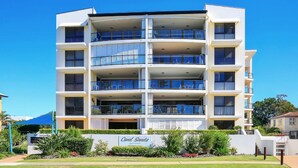 A multi-story residential building with balconies, a sign indicating 'Coral Sands Apartments', and a well-maintained garden in front.