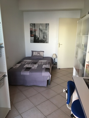 A bedroom with a bed, a cityscape poster, a desk, and a chair.