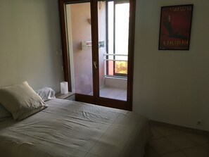 Een slaapkamer met een bed, een kussen, een nachtkastje, een raam en een deur die uitkomt op een balkon.