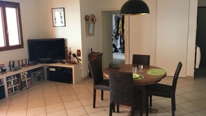 Una sala de estar con televisor, una mesa de comedor con sillas y una cocina visible a través de un vano abierto.