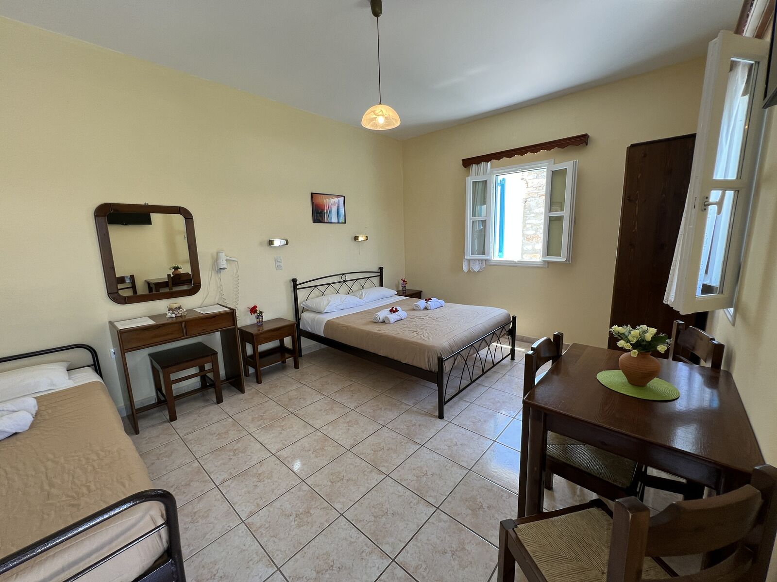 A bedroom with a bed, bedside table, chair, desk, and a dining table with chairs.