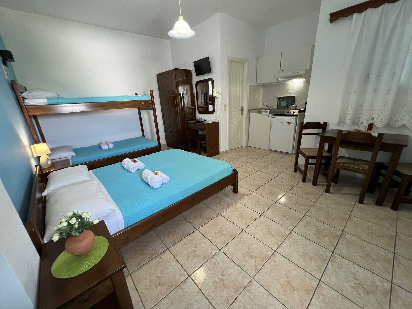 A compact hotel room with a bunk bed, a small kitchenette, a dining table, and a TV.