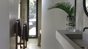 A modern bathroom with a large mirror, a sink, and a potted plant. There is a wooden bench and a door leading to an outdoor area. - Luxury villa. Sea view. Private swimming pool. Independent bedroom and suite. (SAINT MARTIN)