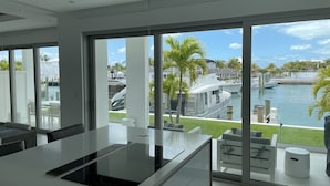 A modern kitchen with a large island, large windows with a view of a marina and boats, and a dining area with white furniture.
