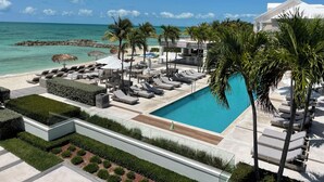 A resort with a pool, lounge chairs, palm trees, and a view of the ocean.