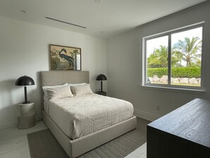 Ein Schlafzimmer mit einem Bett, zwei Nachttischlampen, einem Fenster mit Blick auf Grünflächen und einem Bild an der Wand.