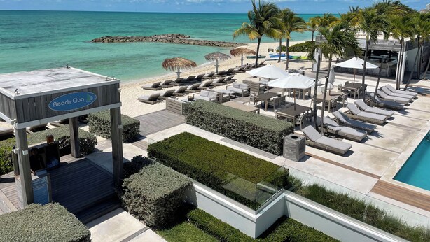 A beach club with lounge chairs, umbrellas, and a pool area.