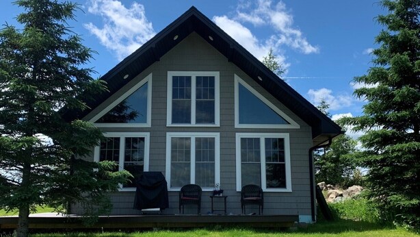 A two-story house with a gabled roof, a front porch with chairs, and a well-maintained lawn. - Snowmobilers Getaway - ATVers Paradise (Caribou)