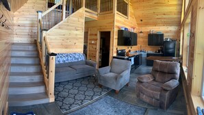 A wooden cabin interior with a staircase, grey sofa, armchair, and brown recliner. - Snowmobilers Getaway - ATVers Paradise (Caribou)