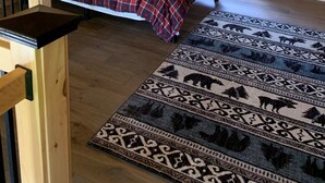A cozy attic bedroom with a wooden sloped ceiling, a bed with a plaid bedspread, a nightstand with a lamp, and a large window with blinds. - Snowmobilers Getaway - ATVers Paradise (Caribou)