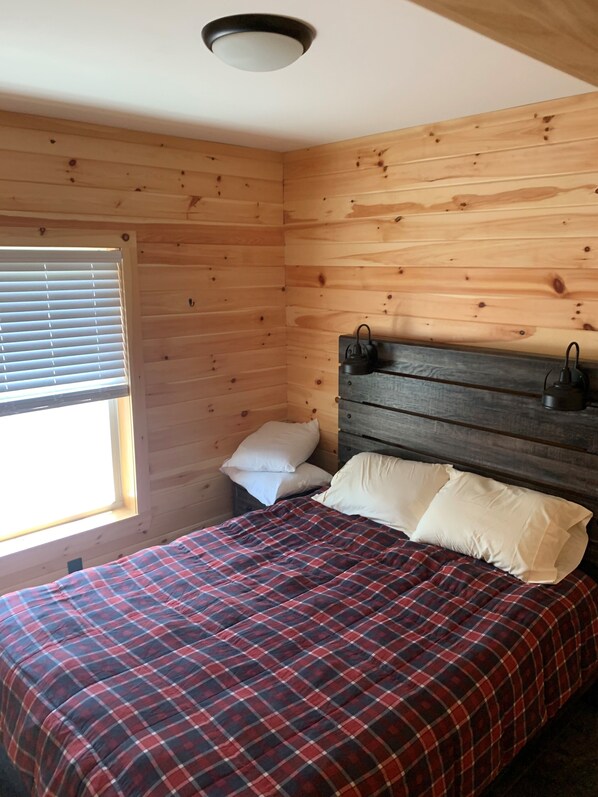 A wooden-paneled room with a bed, a window with blinds, and a ceiling light fixture.
