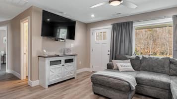 Un salon moderne avec un canapé gris, un meuble de rangement blanc, un téléviseur à écran plat et un ventilateur de plafond.
