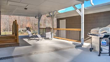 An outdoor covered patio with a grill, seating area, and a view of the surrounding trees.