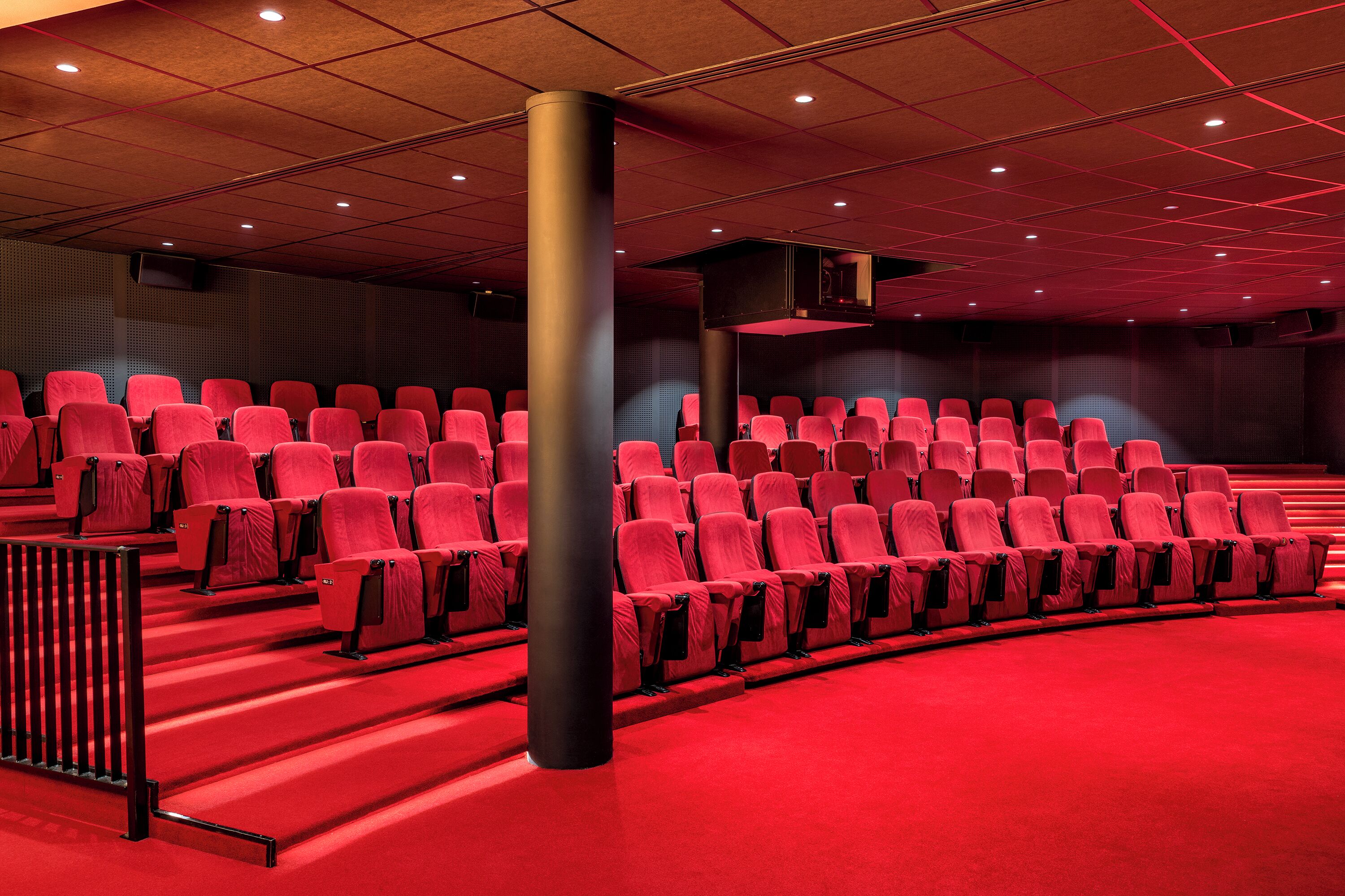 Un cine con hileras de asientos rojos y un suelo cubierto de moqueta roja.