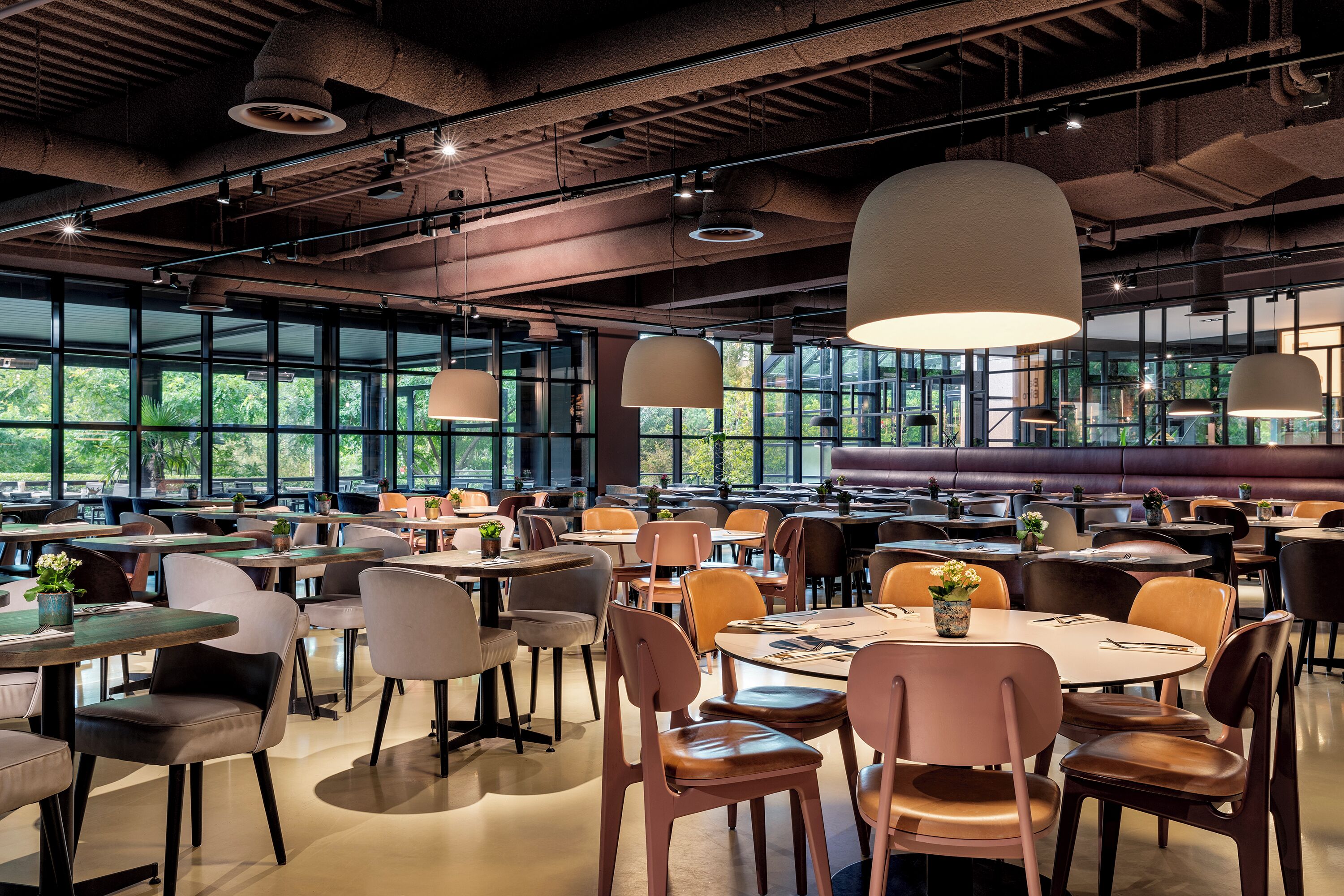 A spacious dining area with multiple tables and chairs, large windows, and hanging pendant lights.
