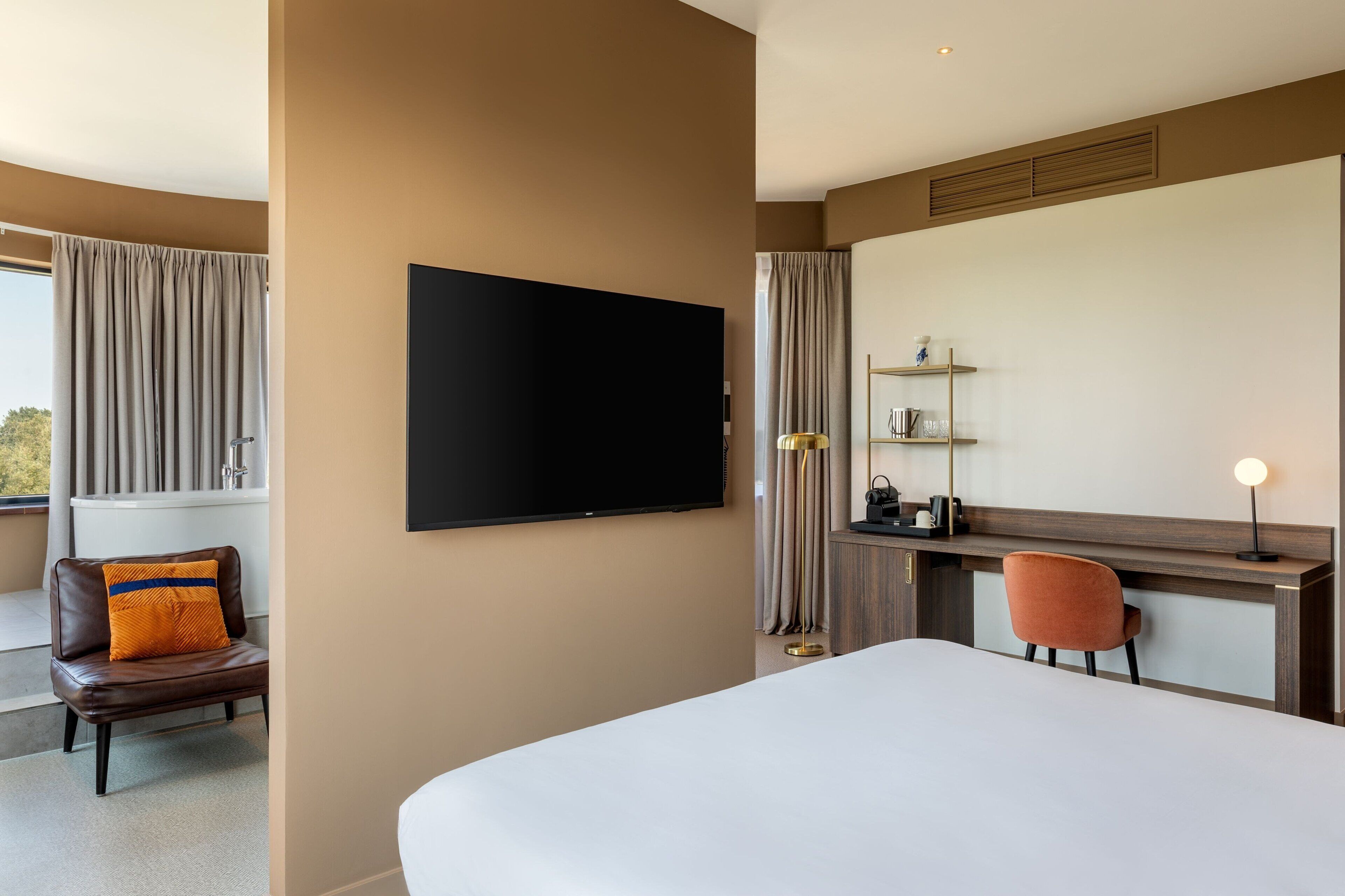 Habitación de hotel con una cama grande, un escritorio con una silla, un televisor de pantalla plana, una ventana con cortinas y vistas al exterior.