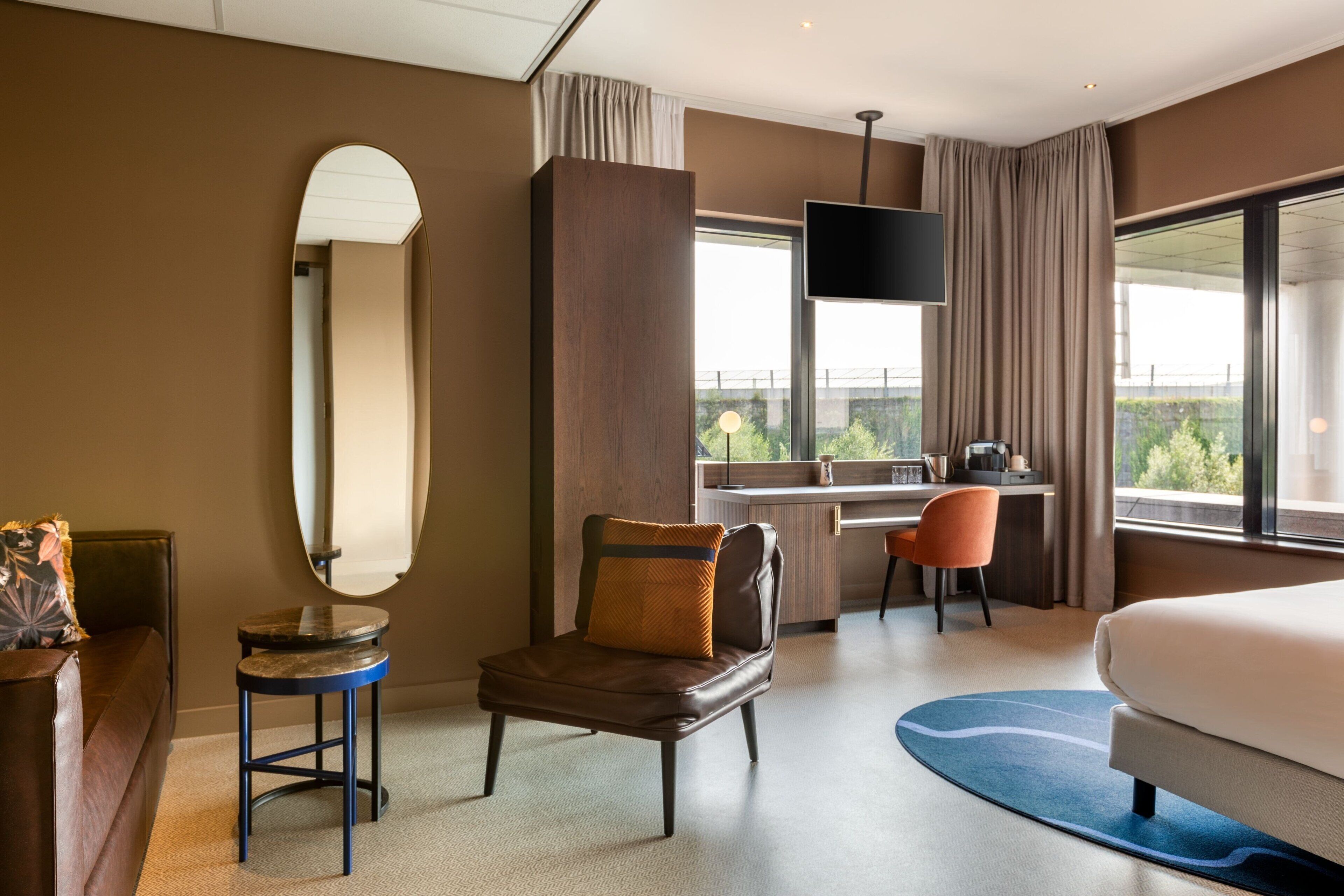 A modern hotel room with a large bed, a desk, a chair, and a TV.