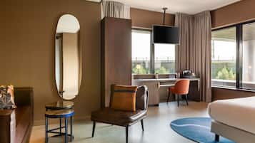 A modern hotel room with a large bed, a desk, a chair, and a TV.