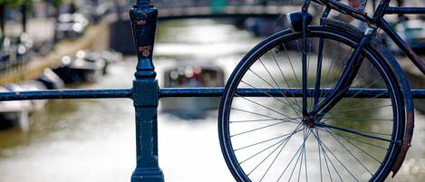 Un vélo appuyé contre une rambarde métallique bleue, au bord d’un canal, avec des bateaux en arrière-plan.
