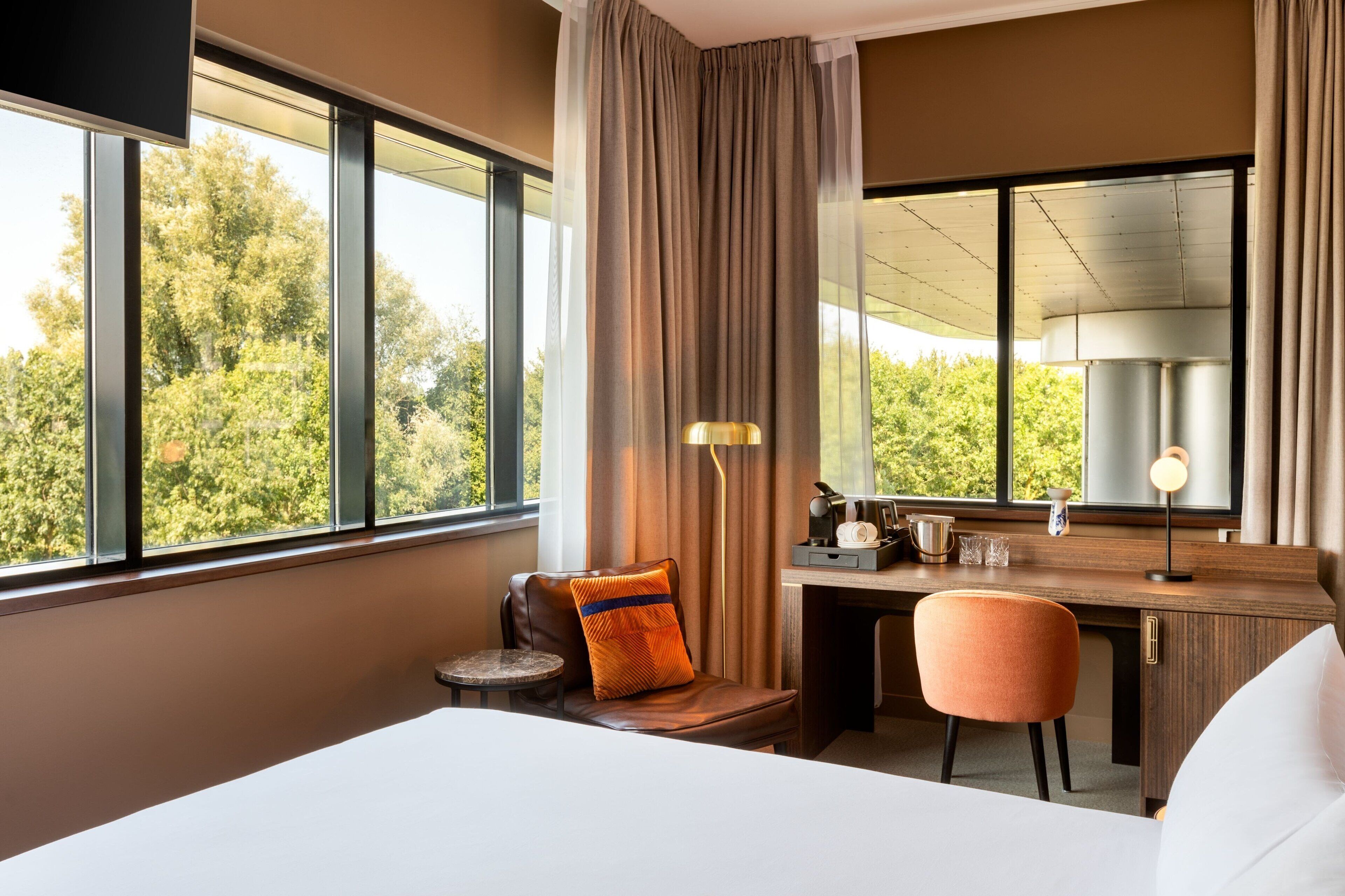 Een hotelkamer met een groot raam, een bureau, een stoel en een bed.
