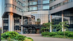 Un hotel moderno con fachada de vidrio, un acceso cubierto y un jardín ajardinado.