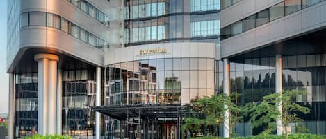 Un hotel moderno con fachada de vidrio, un acceso cubierto y un jardín ajardinado.