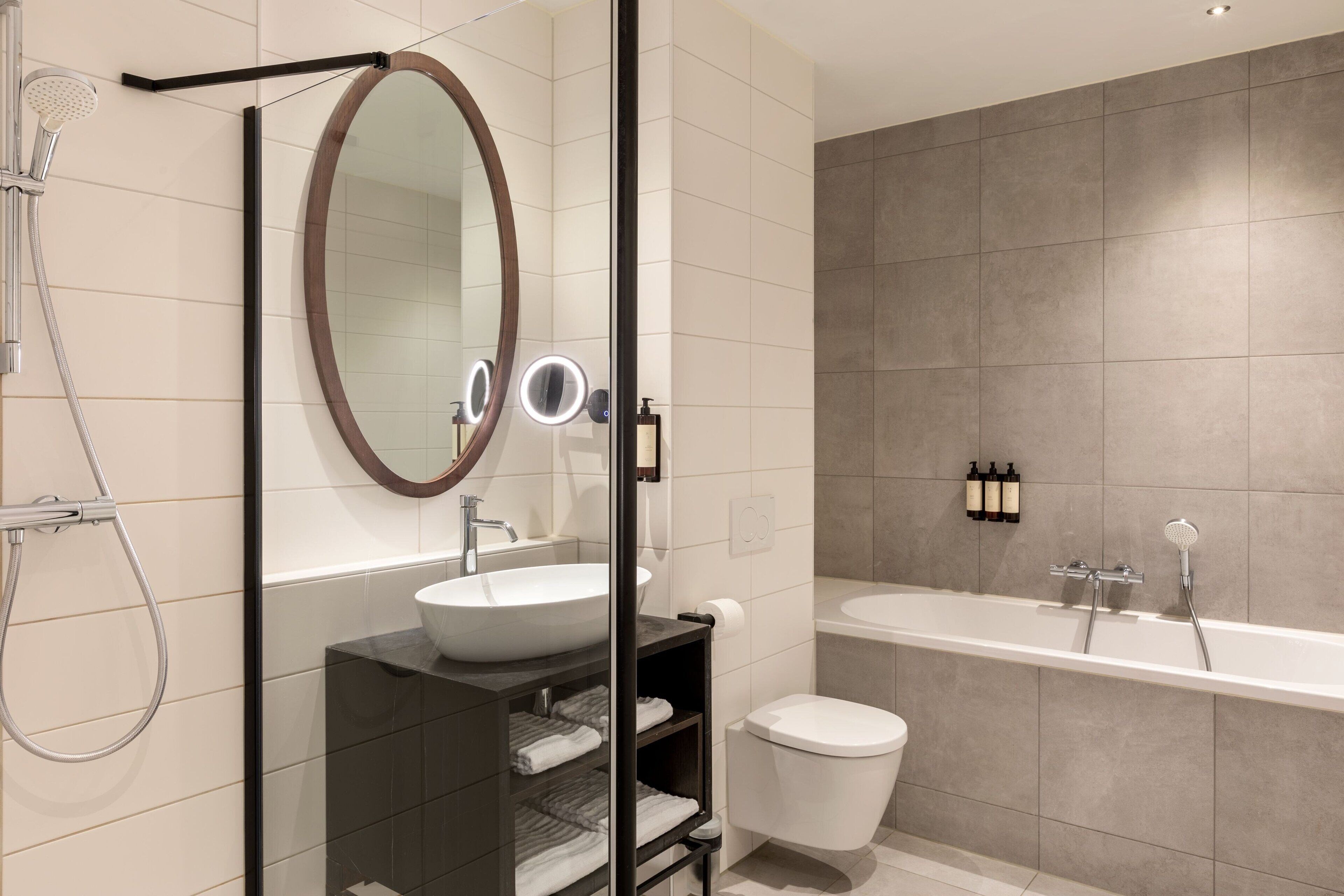 Un baño moderno con cabina de ducha de vidrio, un espejo ovalado grande, un lavamanos blanco y una bañera.