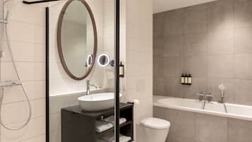 Un baño moderno con cabina de ducha de vidrio, un espejo ovalado grande, un lavamanos blanco y una bañera.