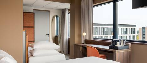 A hotel room with a bed, a desk, a chair, a TV, and a window with a view of buildings.
