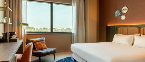 Habitación de hotel con una cama grande, un escritorio con silla, vista a la ciudad y platos decorativos en la pared.