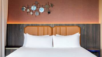 A hotel room with a large bed, two pillows, a headboard, a wall-mounted clock, and a small table.