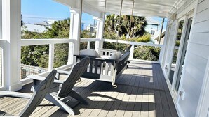 A covered outdoor deck with a swing chair, a table, and a bench. - Walk to tradin post!North cape, private pool, awesome patio & steps to beach! (Port Saint Joe)