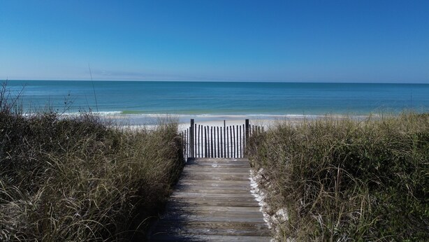 A wooden boardwalk leading to a beach with a wooden fence at the end. - Walk to tradin post!North cape, private pool, awesome patio & steps to beach! (Port Saint Joe)
