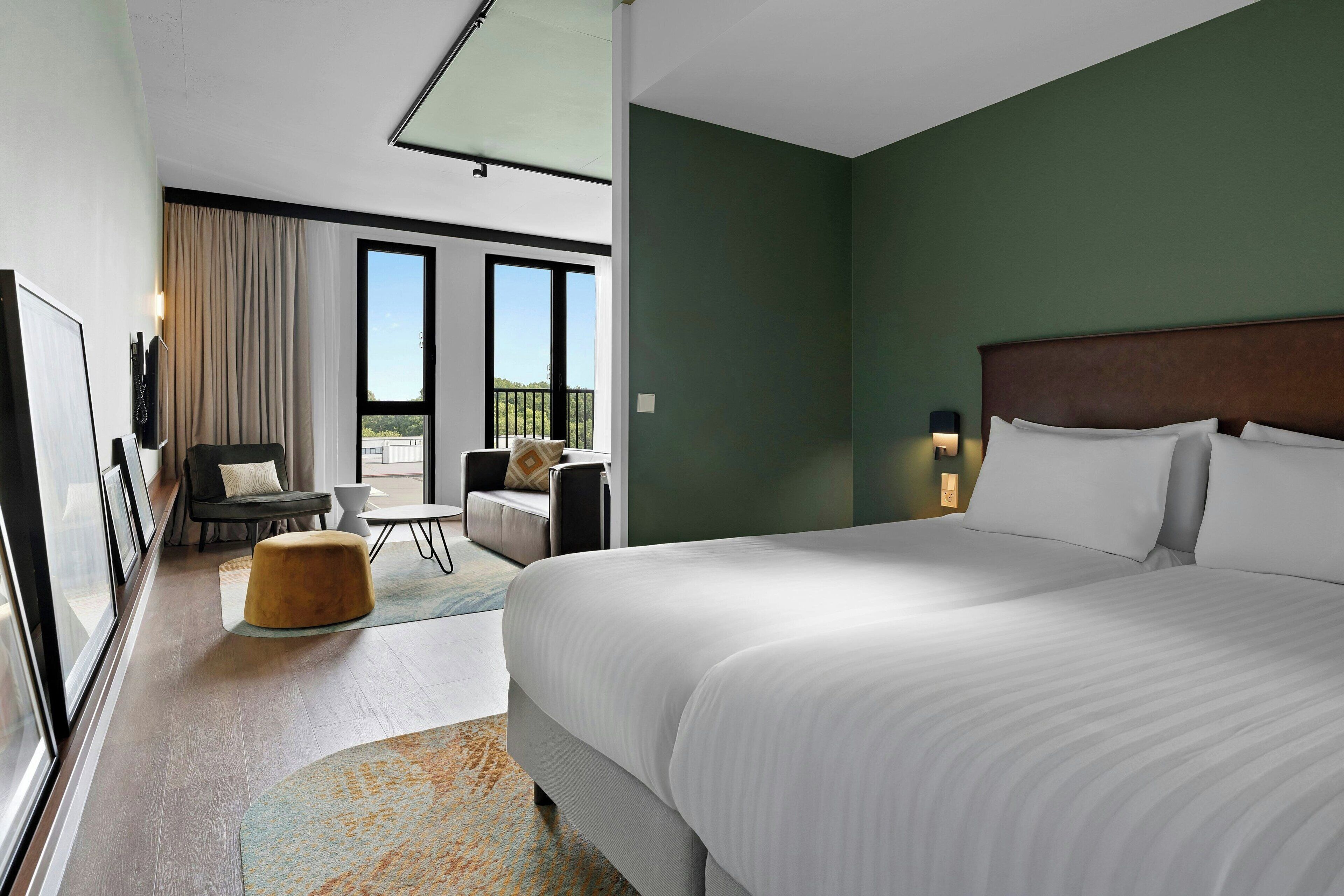 A hotel room with a large bed, a sofa, a small table, and a view of the outdoors.