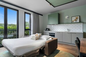 A modern bedroom with a large bed, a small kitchenette, and a balcony with a view of greenery. - Residence Inn by Marriott Amsterdam Schiphol Airport (Badhoevedorp)