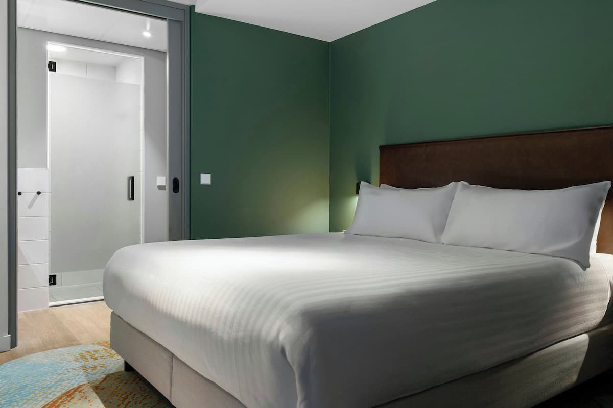 A neatly made bed in a room with green walls and a wooden headboard.