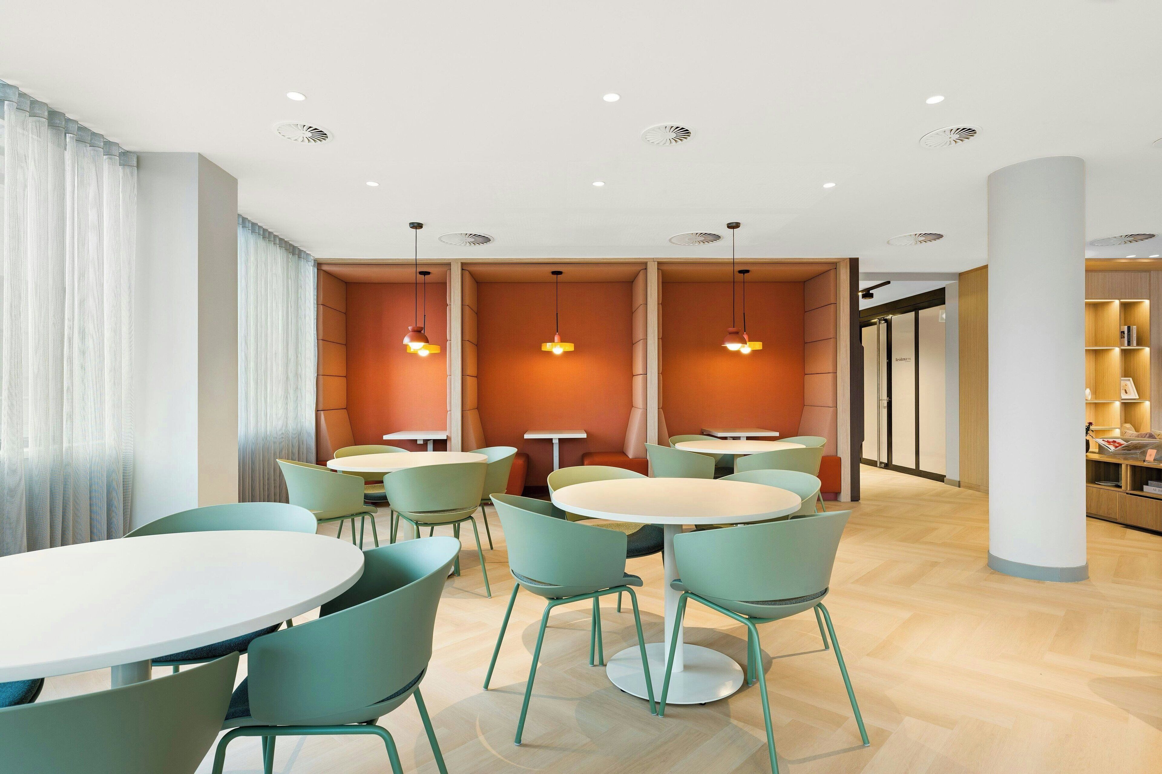 Un espace de restauration moderne avec des tables rondes et des chaises de couleur turquoise, agrémenté de luminaires suspendus et d’un plancher en bois.